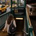 J'ai traversé New York en métro pendant une semaine : mon bilan 8 Une voyageuse descend l'escalier vert d'une station de métro de New York, un sac à dos sur l'épaule, tandis qu'une rame de la ligne R s'approche du quai et que des taxis jaunes circulent en surface.