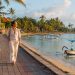 Bali sans scooter : est-ce vraiment possible ? 8 Une jeune femme marche à pied sur la promenade pavée bordée de palmiers le long de la plage de Sanur à Bali, illustrant les alternatives de transport sans scooter.