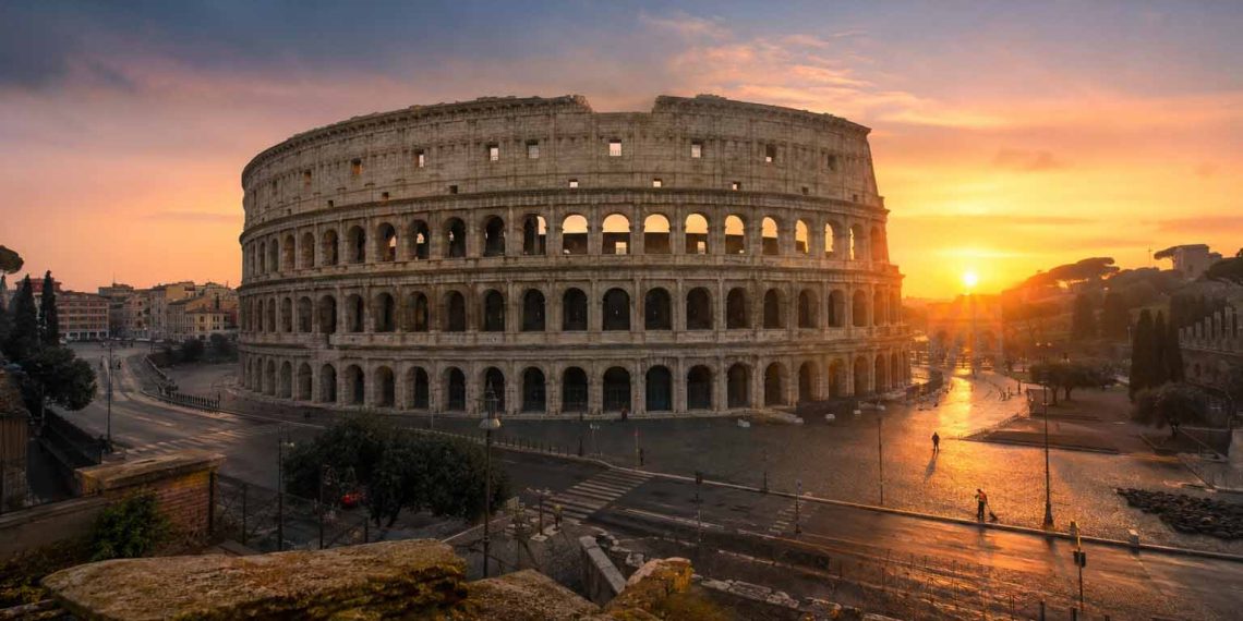 Rome au lever du soleil : les endroits qui m'ont le plus impressionné 1 Vue panoramique du Colisée à Rome au lever du soleil sans aucun touriste, baigné d'une lumière dorée et rose avec de longs reflets sur les pavés.