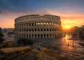 Vue panoramique du Colisée à Rome au lever du soleil sans aucun touriste, baigné d'une lumière dorée et rose avec de longs reflets sur les pavés.