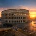 Rome au lever du soleil : les endroits qui m'ont le plus impressionné 6 Vue panoramique du Colisée à Rome au lever du soleil sans aucun touriste, baigné d'une lumière dorée et rose avec de longs reflets sur les pavés.