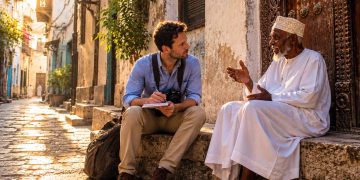 Journaliste de voyage discutant avec un habitant swahili sur un banc traditionnel à Stone Town, Zanzibar.