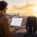 Une voyageuse consulte son budget de voyage sur une tablette face à un panorama urbain au coucher du soleil pour économiser argent voyage.