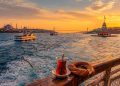 Un ferry municipal navigue sur le Bosphore à Istanbul au coucher du soleil, avec un verre de thé turc et un simit au premier plan, reliant la rive européenne historique à la rive asiatique authentique.