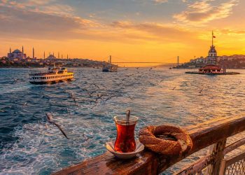 Istanbul des deux côtés du Bosphore : quelle ambiance ai-je préférée ? 4 Un ferry municipal navigue sur le Bosphore à Istanbul au coucher du soleil, avec un verre de thé turc et un simit au premier plan, reliant la rive européenne historique à la rive asiatique authentique.