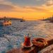Istanbul des deux côtés du Bosphore : quelle ambiance ai-je préférée ? 9 Un ferry municipal navigue sur le Bosphore à Istanbul au coucher du soleil, avec un verre de thé turc et un simit au premier plan, reliant la rive européenne historique à la rive asiatique authentique.