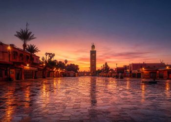 Vue panoramique de la place Jemaa el-Fna vide au lever du soleil à Marrakech avec le minaret de la Koutoubia en arrière-plan.