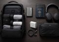 Flat lay artistique des meilleurs accessoires de voyage minimalistes et techniques de 2026 disposés sur une table en bois sombre.