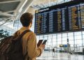 Un jeune voyageur souriant regardant le panneau d'affichage des départs dans un aéroport moderne pour son premier vol en avion.