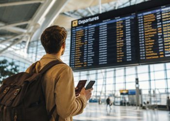 Les erreurs que j'ai faites lors de mon premier vol : Le guide ultime pour votre premier voyage en avion 2 Un jeune voyageur souriant regardant le panneau d'affichage des départs dans un aéroport moderne pour son premier vol en avion.