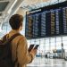 Les erreurs que j'ai faites lors de mon premier vol : Le guide ultime pour votre premier voyage en avion 4 Un jeune voyageur souriant regardant le panneau d'affichage des départs dans un aéroport moderne pour son premier vol en avion.