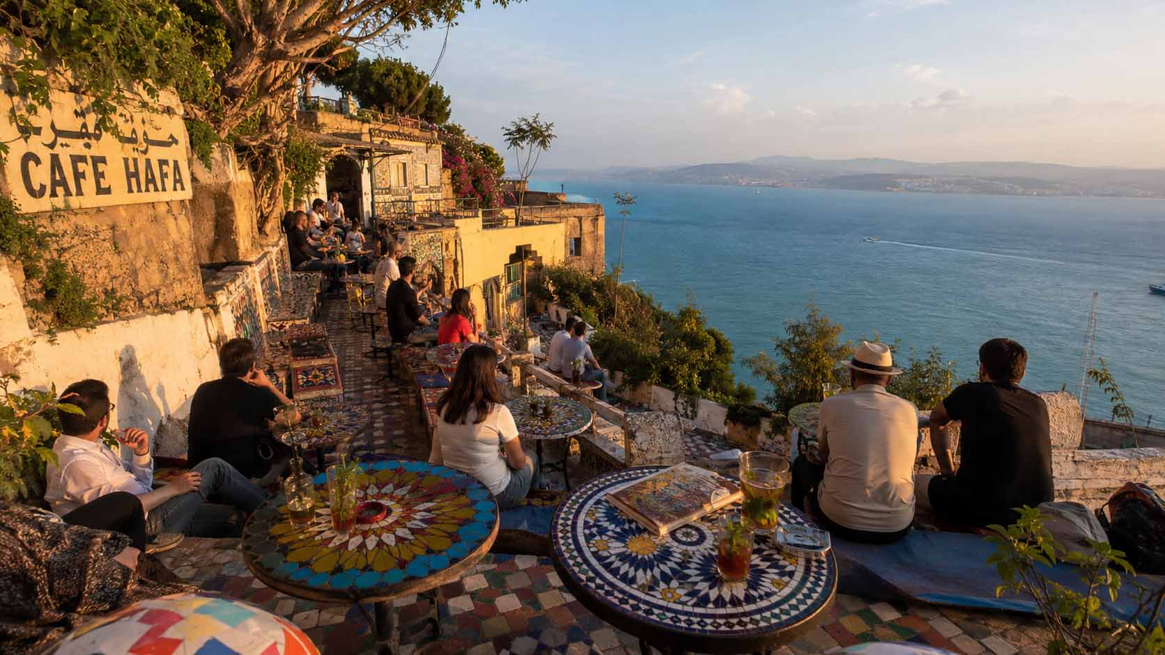Tanger ou Agadir : laquelle choisir pour un premier voyage au Maroc ? 2 Le mythique Café Hafa à Tanger avec des tables en faïence bleue face au détroit de Gibraltar au coucher du soleil.