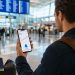 Les alertes de prix valent-elles vraiment le coup ? Mon test sur 6 mois 6 Un voyageur de dos analysant des alertes de prix de billets d'avion sur son smartphone au milieu d'un terminal d'aéroport moderne en 2026.