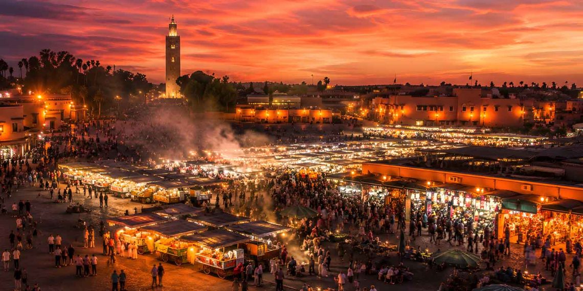 Une semaine à Marrakech : tout ce que j'ai appris (Guide complet, budget et conseils 2026) 1 Vue panoramique de la place Jemaa el-Fna à Marrakech au coucher du soleil avec les stands de nourriture fumants et la mosquée Koutoubia.