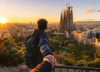 Une voyageuse avec un sac à dos contemple la ville de Barcelone et la Sagrada Família au lever du soleil.