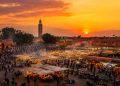Vue panoramique de la place Jemaa el fna à Marrakech au coucher du soleil avec la fumée des stands de nourriture et le minaret de la Koutoubia.