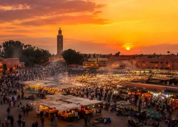 Ce que personne ne raconte sur un voyage à Marrakech 11 Vue panoramique de la place Jemaa el fna à Marrakech au coucher du soleil avec la fumée des stands de nourriture et le minaret de la Koutoubia.