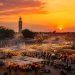 Ce que personne ne raconte sur un voyage à Marrakech 6 Vue panoramique de la place Jemaa el fna à Marrakech au coucher du soleil avec la fumée des stands de nourriture et le minaret de la Koutoubia.