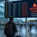 J'ai raté mon avion : voici exactement ce qui s'est passé 3 Un voyageur dépité de dos regardant un panneau d'affichage des vols indiquant l'embarquement clos dans un grand aéroport moderne en 2026.