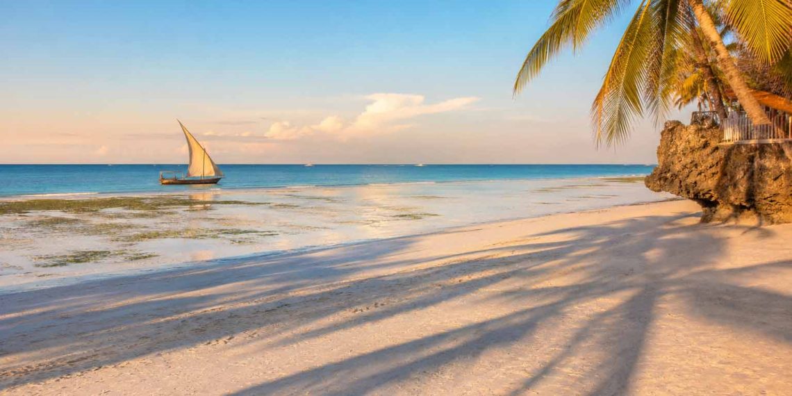 J'ai découvert Zanzibar hors des circuits touristiques : les endroits secrets qui m'ont le plus marqué (Guide 2026) 1 Plage déserte de Zanzibar à marée basse avec un dhow traditionnel au lever du soleil, illustration du voyage hors des sentiers battus.